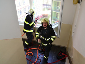 Hasič slaňuje do pátého patra paneláku v Dobiášově ulici.