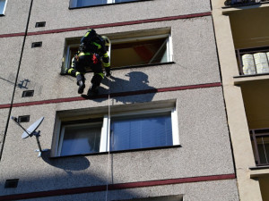 Hasič slaňuje do pátého patra paneláku v Dobiášově ulici.