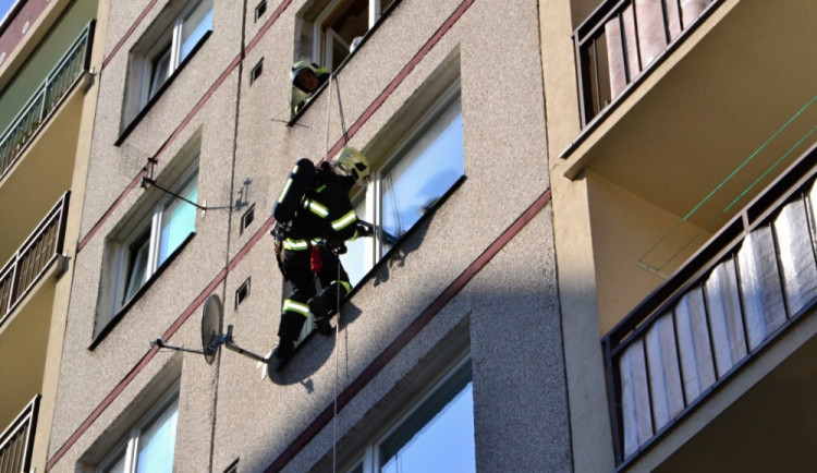 Hasič slaňuje do pátého patra paneláku v Dobiášově ulici.