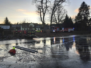 Hasiči se snaží dostat vůz z rybníka.