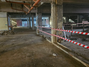 Demolice vnitřních konstrukcí – odhalené nosné sloupy, částečně odstraněné podlahové vrstvy. Plocha je zabezpečena páskami kvůli bezpečnosti pracovníků.