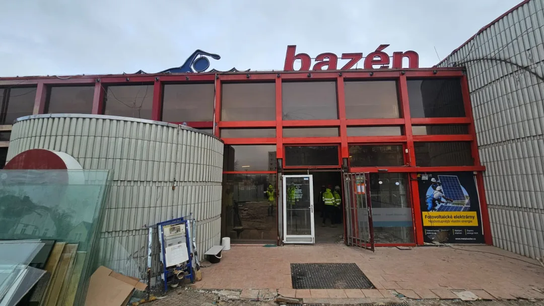 Exteriér bazénu – čelní část objektu má odstraněné vstupní dveře a část fasády. Zahájila se demontáž opláštění budovy. Zmizela také charakteristická "vlnka" nad vstupem, která však nebyla součástí původního návrhu bazénu.