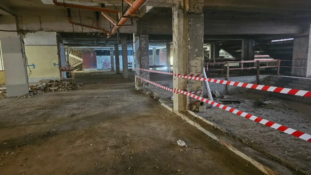 Demolice vnitřních konstrukcí – odhalené nosné sloupy, částečně odstraněné podlahové vrstvy. Plocha je zabezpečena páskami kvůli bezpečnosti pracovníků.