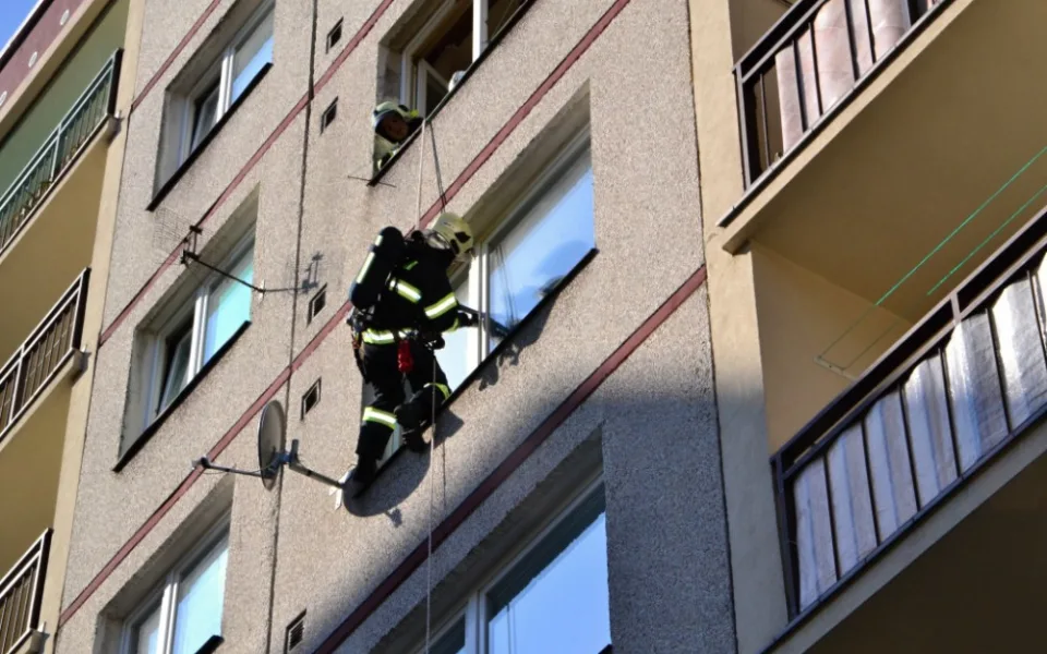Hasič slaňuje do pátého patra paneláku v Dobiášově ulici.